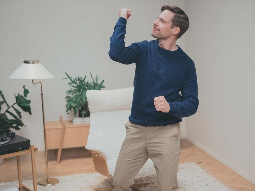 Muž v modrém svetru stojí v dobře osvětlené místnosti, tváří v tvář s klidným výrazem