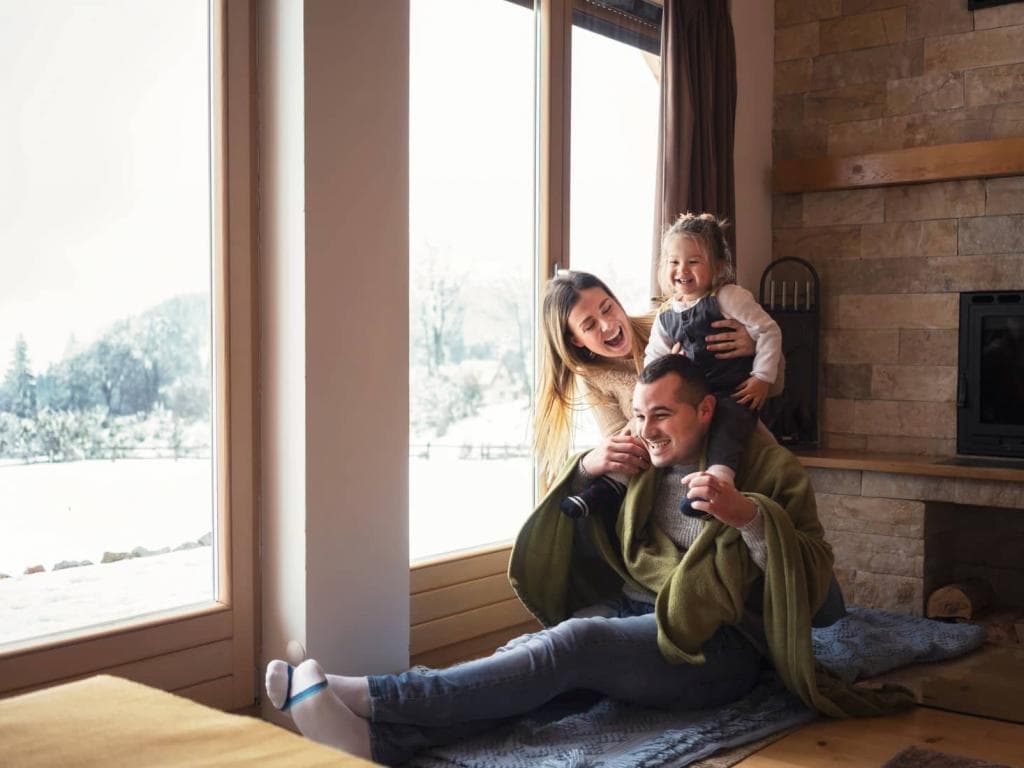 Muž, žena a dítě sedí spolu na gauči, za nimi proudí sluneční světlo oknem