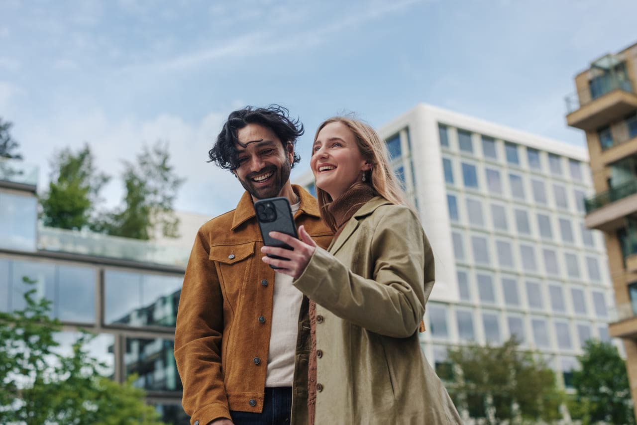 Muž a žena se usmívají, zatímco si dělají selfie před moderní budovou